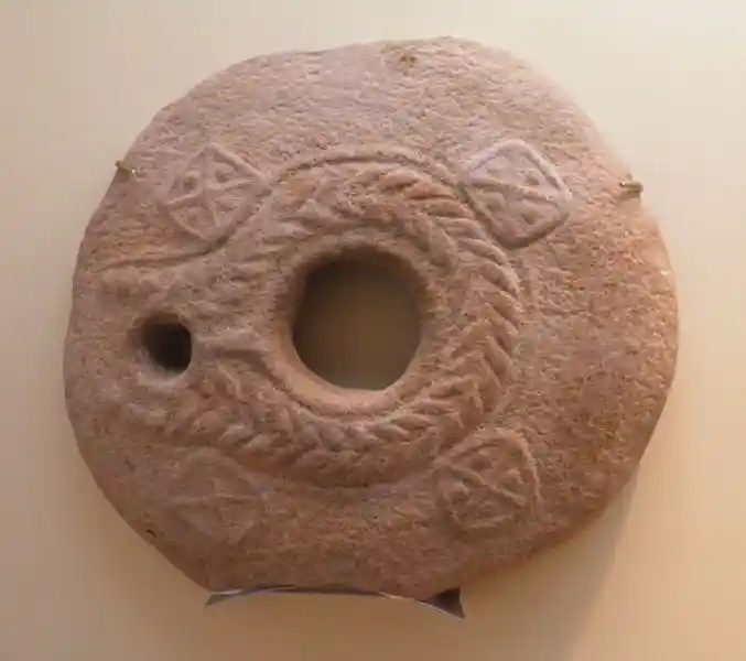 Circular stone with holes and crosses design and a wreath-like symbol